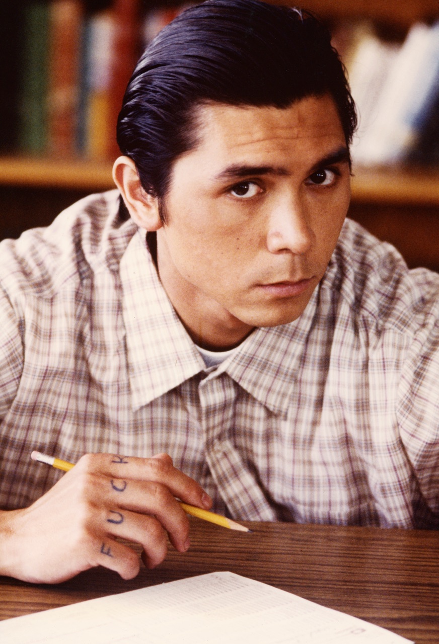 Lou Diamond Phillips as Angel Guzman in Stand and Deliver, seated at a school desk holding a pencil