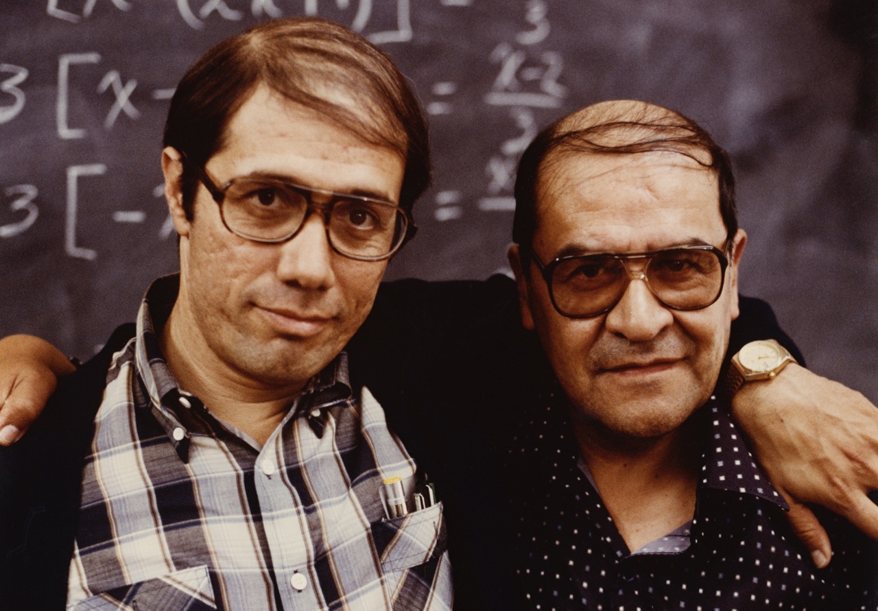 Edward James Olmos, in character as Jaime Escalante, standing with the real Jaime Escalante in front of a chalkboard covered in calculus equations